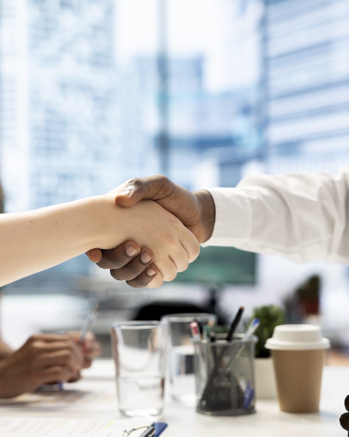 Apretón de manos sobre una mesa de reuniones, con la ciudad al fondo